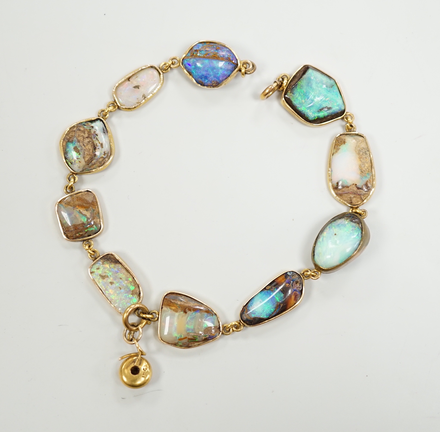 An early 20th century yellow metal and opal set bracelet, of various shapes and hung with central 15ct and diamond chip set charm, 21cm, gross weight 15 grams.